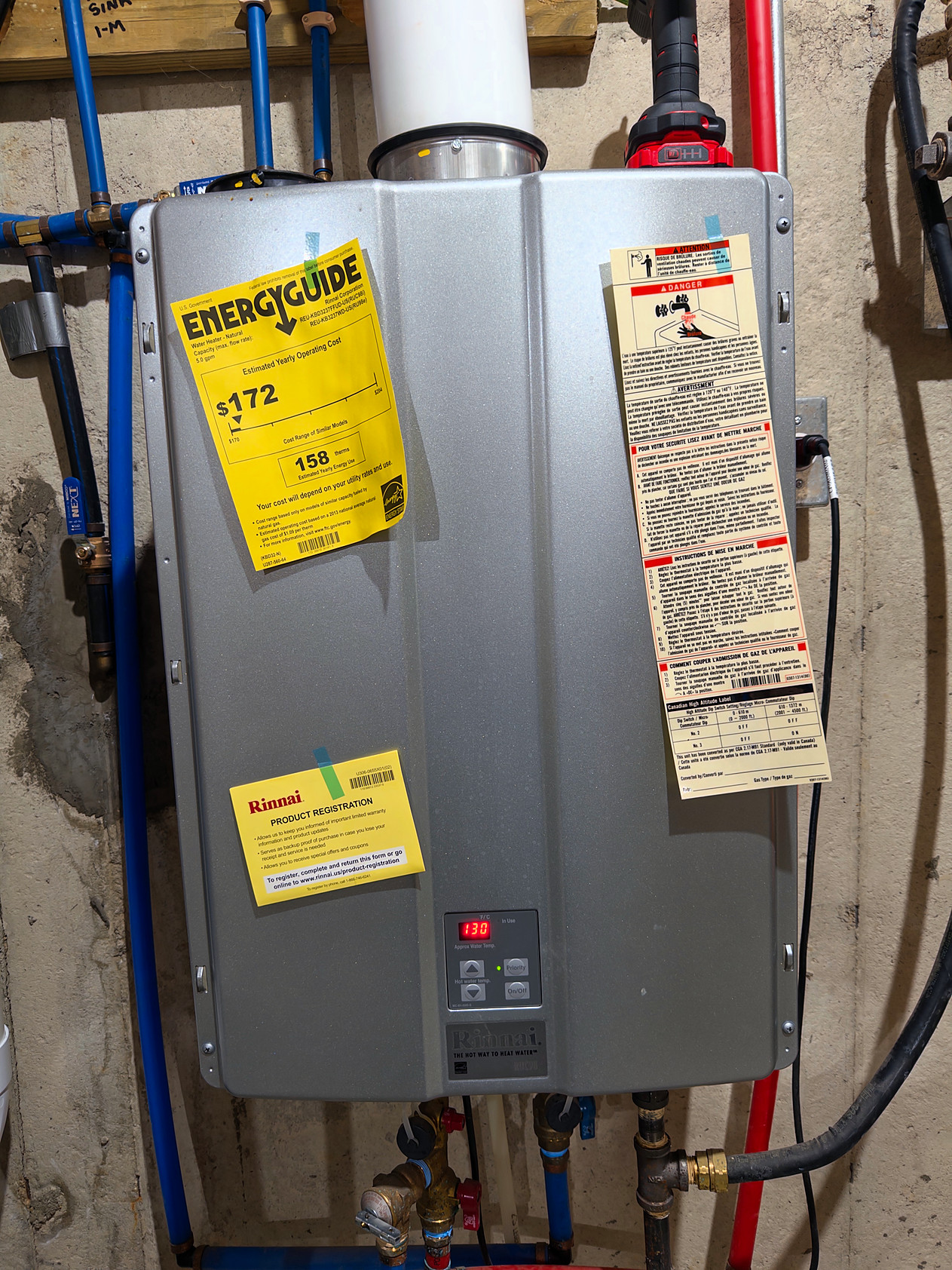 Rinnai RUC98 tankless water heater on a basement wall, with its control panel showing 130