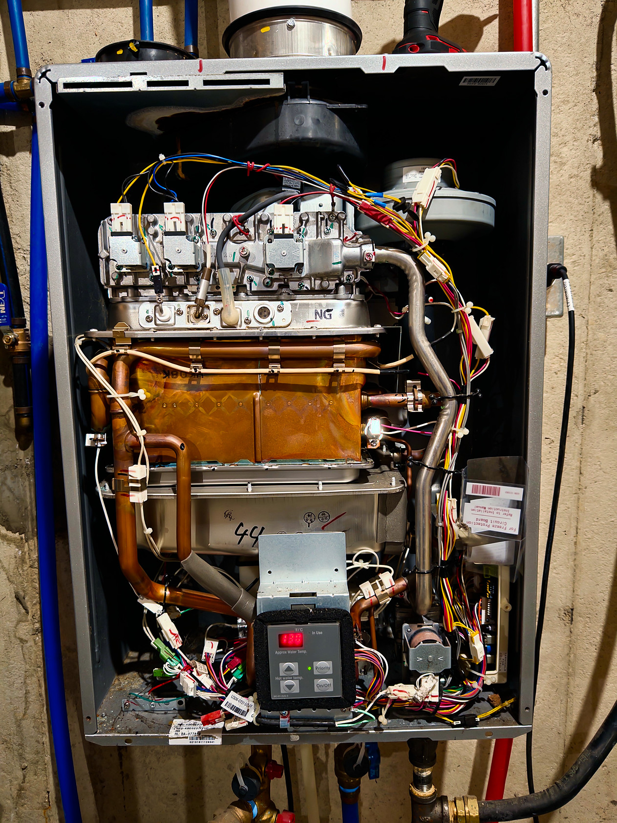 Inside the Rinnai RUC98 with the front cover removed: gas valve assembly, copper heat exchanger, fan, circuit board, and bundles of wiring